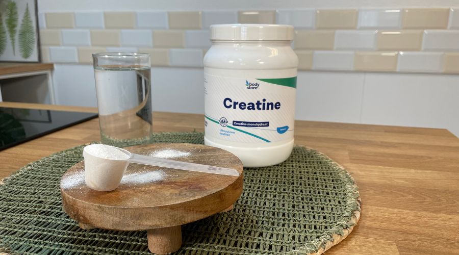 een pot creatine monohydraat poeder, een scoop creatine en een glas water